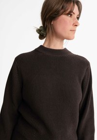 Dunkelbrauner Strickpullover mit einer strukturierten, gerippten Optik, der einen hohen Kragen und lange Ärmel hat. Der Stoff hat ein weiches, dickes Aussehen.