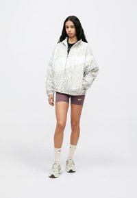 Ελαφρύ μπουφάν με φερμουάρ σε μπεζ και λευκό με μοτίβο λεοπάρ. Διαθέτει ψηλό γιακά και ελαστικά μανσίκια, συνδυασμένο με σκούρα σορτς.