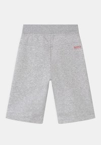 Světle šedé kraťasy až ke kolenům s elastickým pasem, měkkou texturou tkaniny a malým červeným logem "BOSS Hugo Boss" v pravém horním rohu.