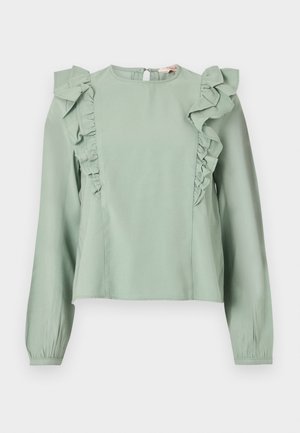 Helehelekollane pika varrukaga pluus, millel on frontaalkülgedel ja õlgadel volangid, ümmargune kaelus ja tagaküljel nööpidega kinnitus.