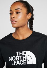 Sweatshirt preto com decote redondo canelado e grande logótipo branco "THE NORTH FACE" na frente. Tecido suave e corte descontraído.