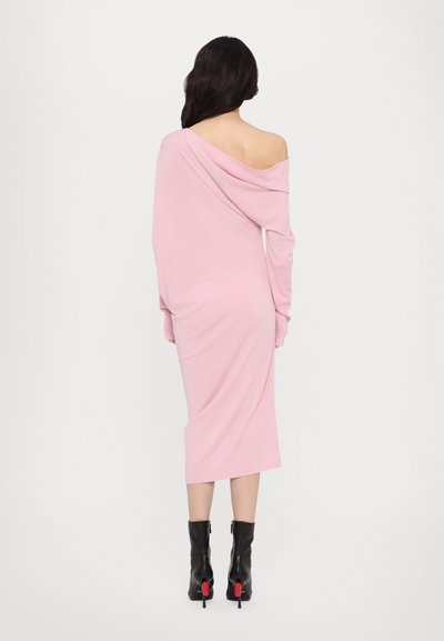 Rochie lungă, ajustată, cu umerii goi, dintr-un material roz moale, cu mâneci lungi și tiv până la jumătatea gambei. Pur corectă cu cizme negre până la gleznă cu accente roșii.