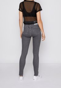 Černý průhledný top v kombinaci s úzkými šedými džíny. Džíny mají klasický pětikapsový design s detaily šití a slim fit.