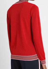 Roter Pullover mit strukturiertem Finish, ausgestattet mit einem gestreiften Kragen und Saum in Marineblau, Weiß und Rot. Lange Ärmel, taillierter Schnitt.