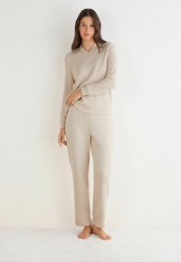 Beige ribbed loungewear set met een V-hals lange mouwen top en bijpassende broeken. Zachte textuur, ontspannen pasvorm en geen zichtbare patronen.