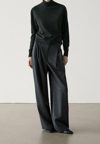 Pull col roulé ajusté vert foncé associé à un pantalon taille haute à larges jambes à fines rayures gris foncé. Chaussures noires à bout pointu.