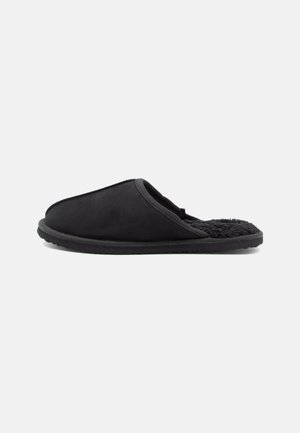 Fekete slip-on papucs bolyhos béléssel és puha talppal, profilból bemutatva fehér háttér előtt.