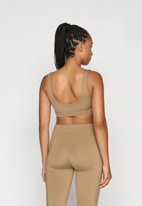 Μπεζ αθλητικό σουτιέν με χαμηλή πλάτη, φαρδιές τιράντες και ταιριαστά ψηλόμεσα κολάν, φτιαγμένα από λεία και ελαστική ύφανση.