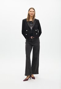 Czarna krótka marynarka z srebrnymi guzikami, czarny t-shirt z grafiką, szare dżinsy z wysokim stanem i szerokimi nogawkami oraz bordowe buty na obcasie.