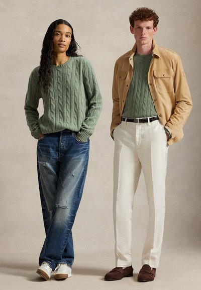 Due modelli indossano maglioni verdi abbinati con trecce; uno li abbina a jeans strappati e sneaker, l'altro a pantaloni bianchi, giacca color cammello e mocassini.