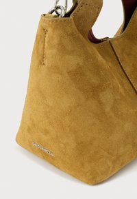 Borsa a secchiello in camoscio color pelle di daino con dettagli in argento e piccolo logo del marchio in metallo nell'angolo inferiore anteriore.