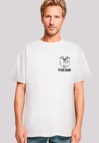 Weißes Baumwoll-T-Shirt mit einem grafischen Druck eines offenen Buchs auf der Vorderseite und dem Text "WEISER VATER" in Schwarz. Lockerer Schnitt und kurze Ärmel.