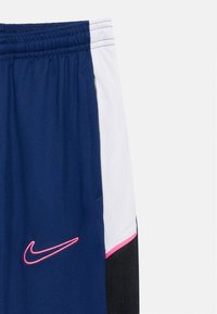 Μπλε αθλητικές σορτς με λευκές και μαύρες πλαϊνές λωρίδες, ροζ περιθώριο και ροζ λογότυπο Nike swoosh κοντά στην τσέπη.