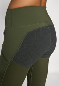 Olivgröna leggings med hög midja och svart strukturpanel. Har platta sömmar och en liten svensk flagga som accent.