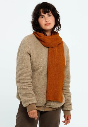Bruine fleece trui met een oranje geribde sjaal die om de nek valt. De sjaal is zacht en de trui heeft een textuur die een warme uitstraling geeft.