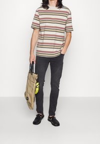Pruhované tričko v odstínech tan a burgundy, černé slim džíny, černé tkané boty a hnědá taška se žlutým popruhem. Jednoduchý neformální outfit.