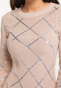 Maglione lavorato a maglia rosa chiaro con un motivo a diamante fatto di paillettes colorate. Collo rotondo e polsini a coste. Tessuto morbido e testurizzato.