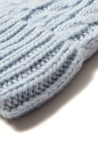 Berretto lavorato a maglia di colore azzurro chiaro, caratterizzato da motivi a coste texturizzati, filato spesso e un aspetto morbido e peloso. I bordi sono leggermente arrotolati.
