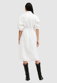 Weißes Jeanshemdkleid mit Puffärmeln, tailliertem Design und mittellanger Schnittführung. Getragen mit schwarzen Cowboy-Stiefeln.