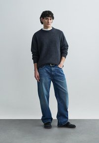 Dark gray sweater, blue jeans, and black shoes. Sweater has a round neckline and ribbed cuffs. Jeans are loose-fitting with a faded finish.