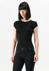 T-shirt nera a maniche corte con scollatura rotonda, realizzata in tessuto elasticizzato. Indossata con jeans neri aderenti caratterizzati da discreti dettagli in rosso.