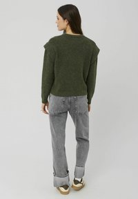 Pull en tricot vert à manches courtes et coupe décontractée, associé à un jean large gris clair et des baskets basses.