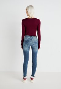 Burgunderfarget langermet topp parret med falmede blå denimjeans og hvite sneakers med røde detaljer. Har en tettsittende design og lett frynsete kanter.