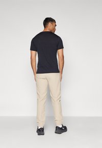 Marineblauwe t-shirt met korte mouwen, gecombineerd met beige broek met elastische manchetten en zwarte sportschoenen, gezien vanuit de achterkant.