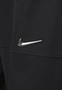 Svarta idrottsbyxor med en skinande silverfärgad Nike-swoosh-logotyp på sidan, med en slät tygstruktur och strömlinjeformat design.