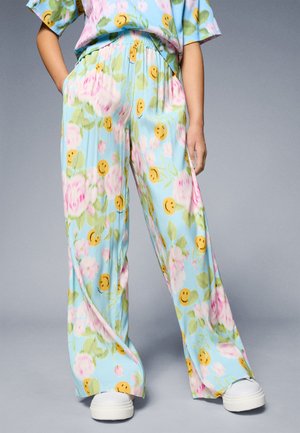 Luchtige, lichtblauwe broek met een bloemenpatroon, versierd met gele glimlachende gezichten en roze bloemen. Heeft een elastische tailleband en een losse pasvorm.