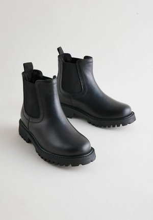 Crne kožne Chelsea čizme s elastičnim bočnim panelima i debelim potplatima, prikazane na svijetloj pozadini, ističući njihov elegantan dizajn.