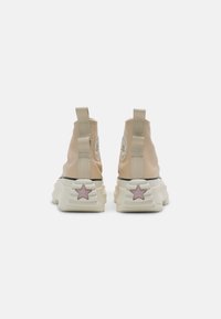 Beige hoge sneakers met dikke witte zolen, achteraan trekbandjes en roze sterdetails op de hielen, afgebeeld tegen een effen witte achtergrond.