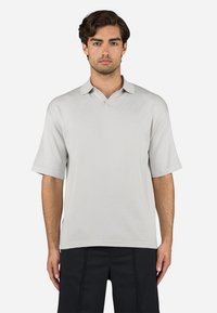 Polo de manga curta cinza claro com decote em V, textura suave e detalhe de logótipo subtil. Barra reta e ajuste descontraído.