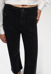 Czarne, krótkie spodnie denimowe z wysokim stanem, dwoma przednimi kieszeniami z klapką i czarnymi elementami metalowymi. Gładka faktura i prosty krój nogawek.