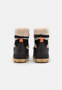 Bottes noires avec une tige en fourrure, accents orange et lacets à motifs. Elles comprennent une semelle en caoutchouc texturée et un logo sur le talon.
