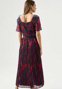 Blumenkleid in Maxi-Länge mit kurzen Ärmeln, runder Rückenpartie, plissiertem Stoff und einem lebhaften mehrfarbigen Muster auf dunklem Hintergrund.