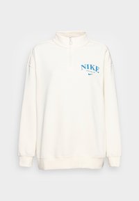 Vit fleece zip-up sweatshirt med hög krage, med en blå "NIKE" logotyp och enkel konstruktion. Mjuk textur och avslappnad passform.