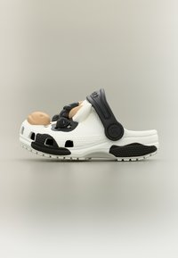 Λευκό κλογκ με μαύρο λουράκι και υφασμένα μαύρα στοιχεία, με τρισδιάστατο σχέδιο αγελάδας στο επάνω μέρος.