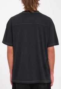 Zwarte T-shirt met korte mouwen en groene contrasterende stiksels, met een effen achterkant en een subtiele grafische detay aan de zijkant.