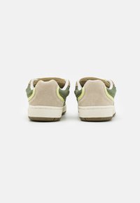 Zapatillas con un upper de ante beige, acentos de malla verde y una media suela blanca. El talón presenta un detalle amarillo y una suela texturizada.