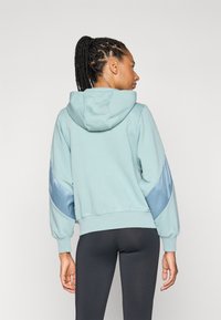 Lyseblå hettegenser med snor i hetta, satengblå detaljer på ermene, ribbestrikkede mansjetter og en avslappet passform. Brukt med svarte leggings.