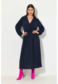 Navy-Blaues Langarmkleid mit tailliertem Schnitt und V-Ausschnitt, das eine fließende Passform hat. Kombiniert mit leuchtend pinken Ankle Boots für einen Kontrast.