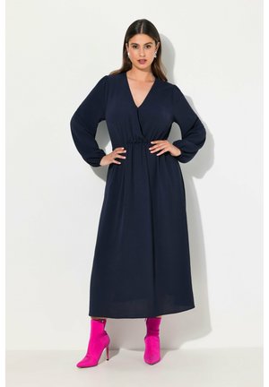 Marineblauwe lange jurk met een strakke taille en V-halslijn, met een vloeiende pasvorm. Gecombineerd met levendige roze enkellaarsjes voor contrast.