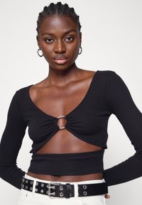 Top cropped preto de mangas longas com um detalhe em anel prateado redondo, apresentando um corte em V profundo e material franzido na frente. Tecido texturizado.