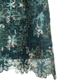 Koronkowa tkanina w kolorze morskim z różnymi odcieniami; posiada delikatną falowaną krawędź. Na dole znajduje się srebrna metka z logo "GUESS".
