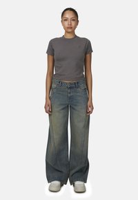 Grijze getailleerde t-shirt met ronde hals, gecombineerd met wijde blauwe denim jeans met een vervaagde textuur en contrasterende stiksels. Witte sneakers.