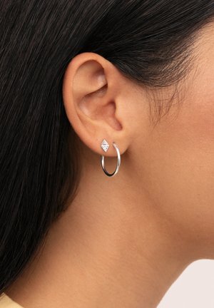 Pendientes de aro de plata con un pequeño stud triangular que presenta una superficie texturizada y un acabado brillante, usados en el lóbulo.
