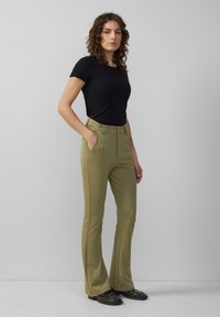 T-shirt noir ajusté à manches courtes effilochées associé à un pantalon flare vert olive avec deux poches avant et une fermeture éclair.