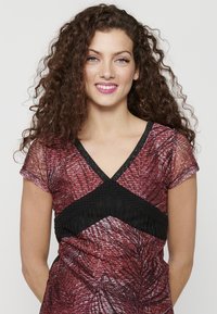 Top a fantasia rossa e nera con scollatura a V, maniche corte e banda nera texturizzata sotto il busto. Materiale morbido e leggero.