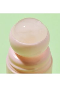 Rund, glansig topp med en ljusrosa bas. Behållaren har en slät yta med subtila åsar. Bakgrunden är i en mjuk grön nyans.